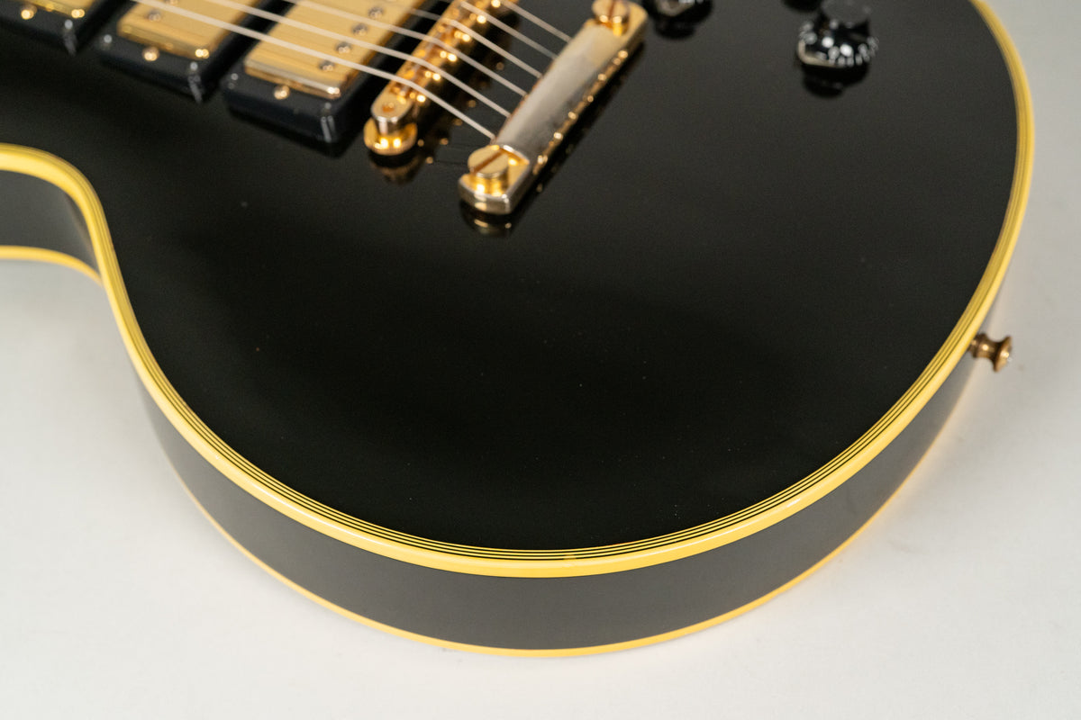 Close-up of the guitar's lower bout, showing the glossy black finish, multi-ply cream binding, and gold bridge with light wear.