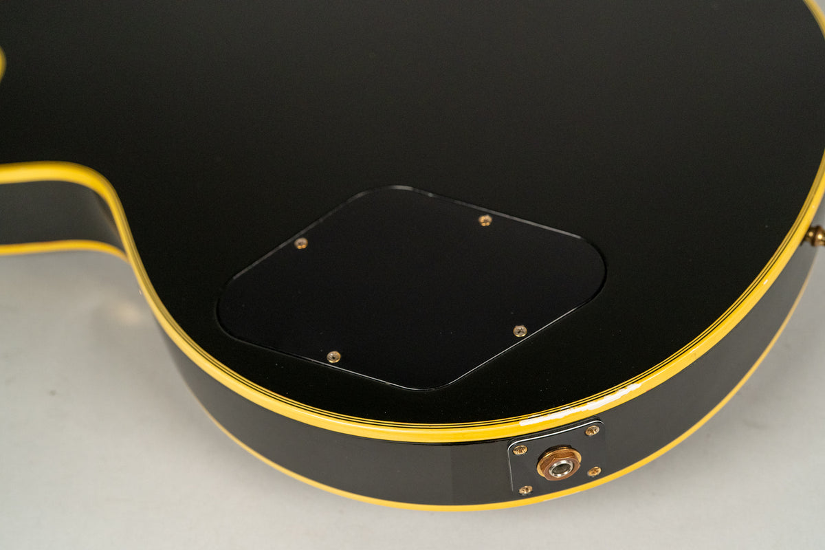The guitar's black back with yellow binding is shown, featuring a control cavity cover and an output jack with minor finish wear.