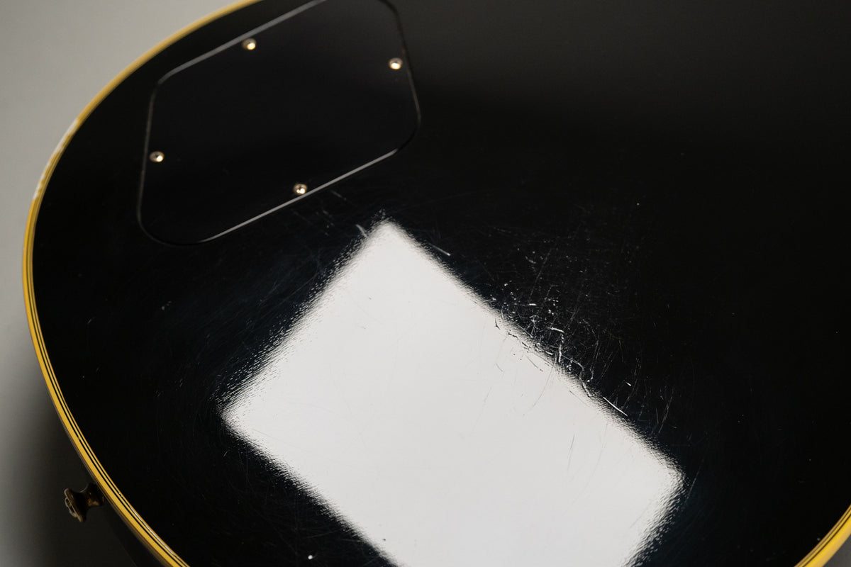 Close-up of the guitar's black back, showing a control cavity cover, yellow binding, and heavy surface scratches and finish checking.
