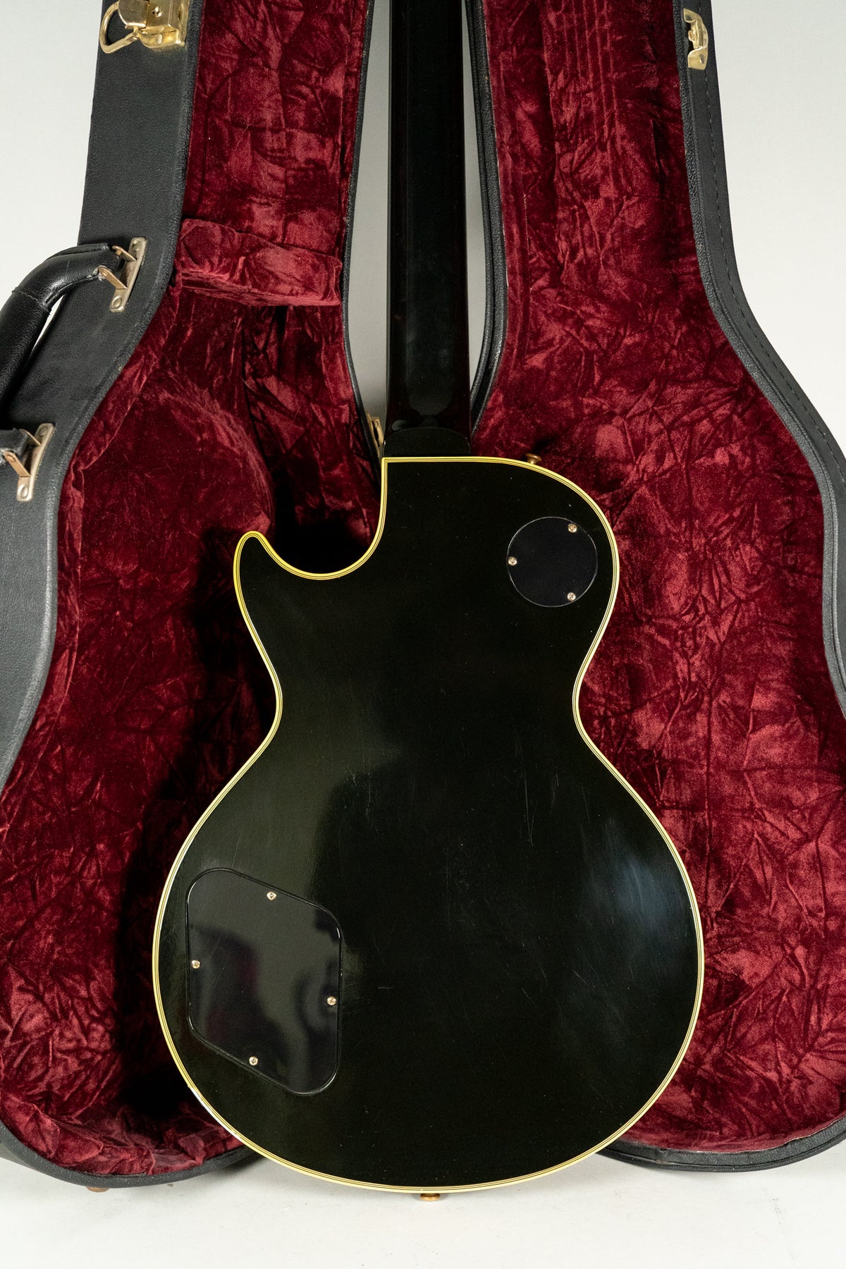 The guitar's glossy black back, with cream binding and two control plates, rests in a red velvet-lined open hard case.