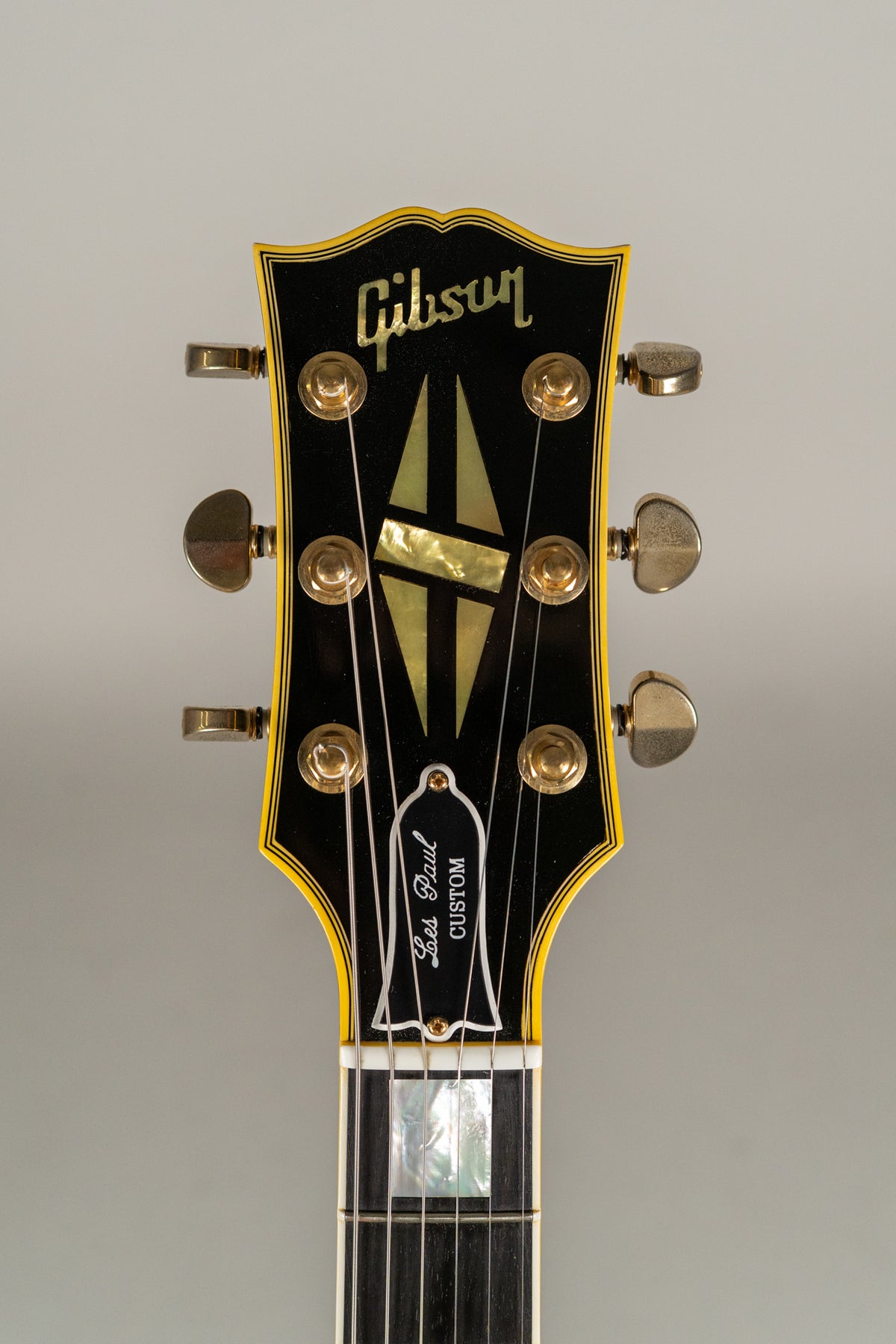 Close-up of the black headstock with gold tuners, multi-ply binding, and mother-of-pearl split diamond inlay.