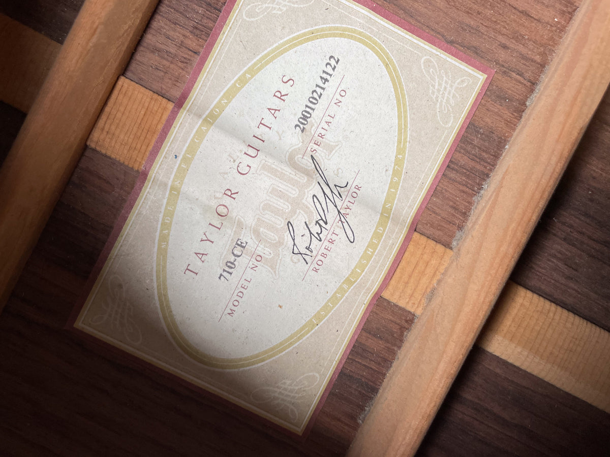 The guitar's interior, showing the light-colored label with red trim and dark wood bracing, is dusty.