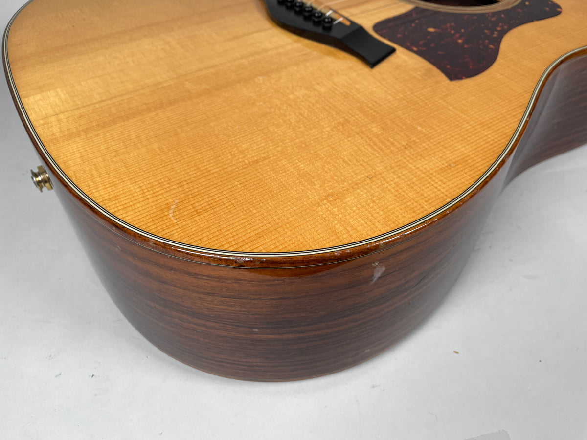 Close-up of the natural finish acoustic guitar's lower bout, showing light wear and dings on the dark wood side and binding.