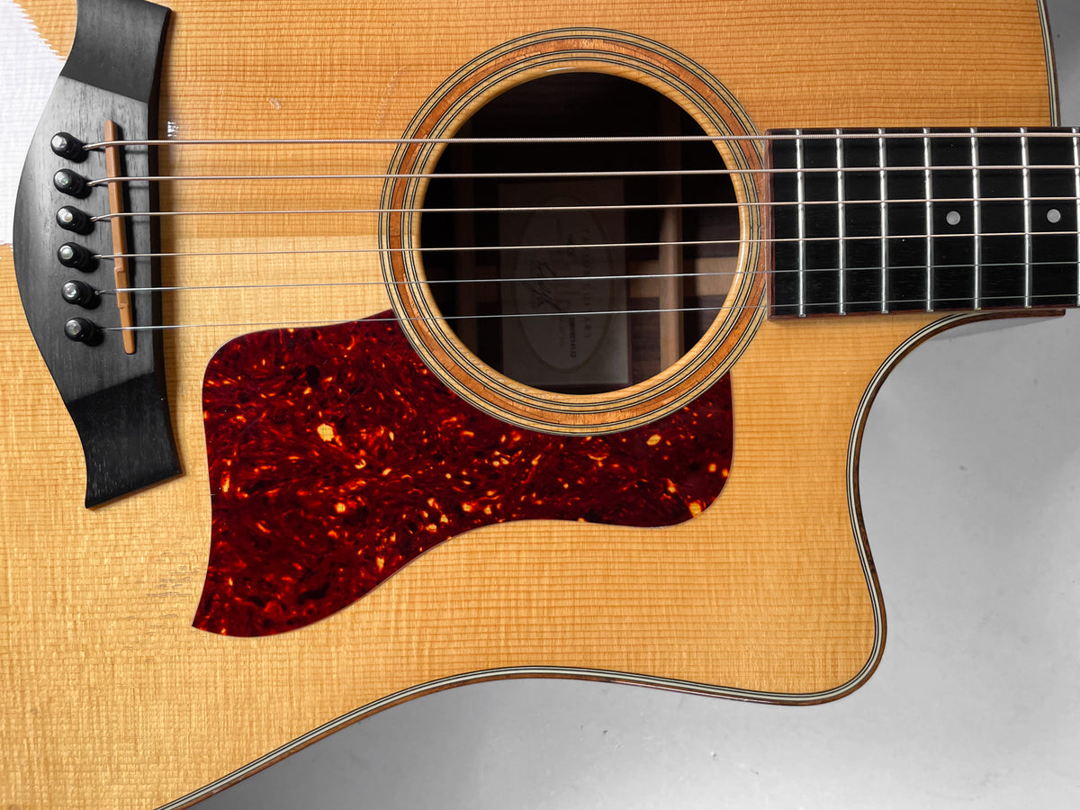 Close-up of the natural finish acoustic guitar's upper body, showing the soundhole, tortoise pickguard, bridge, and cutaway.