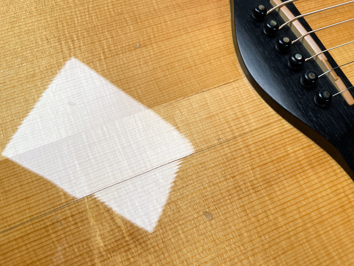 Close-up of the natural finish spruce top, showing the black bridge with six bridge pins and a bright reflection on the lower bout.
