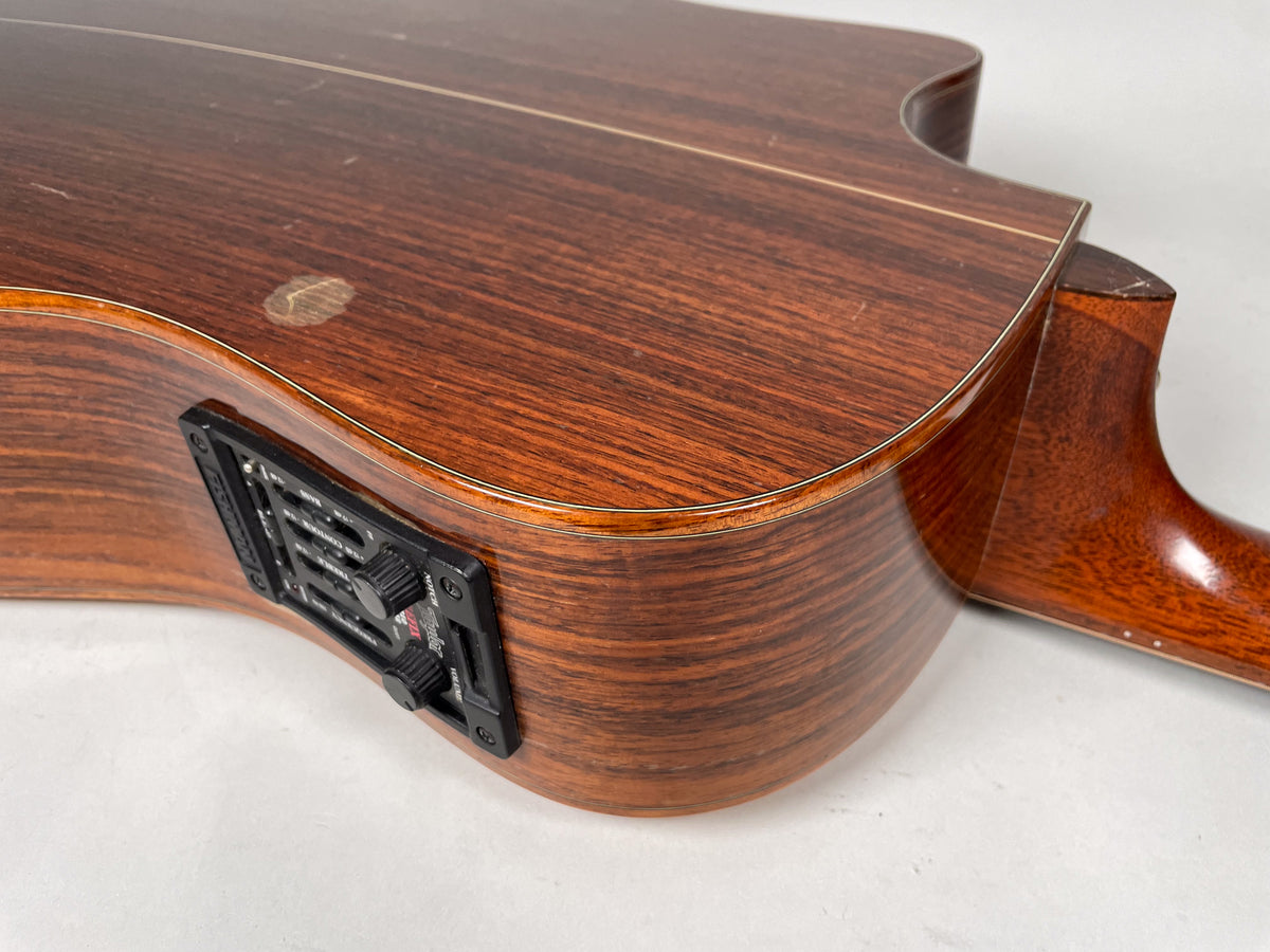 Close-up of the guitar's lower bout, showing the dark wood grain, built-in preamp with controls, and light wear on the body and neck heel.