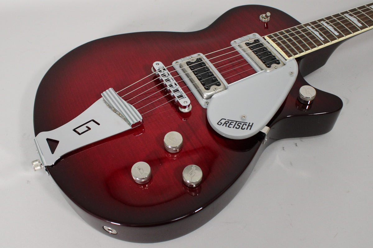 The transparent red guitar body, with a dark burst edge, features chrome hardware, a silver pickguard, and three silver control knobs.