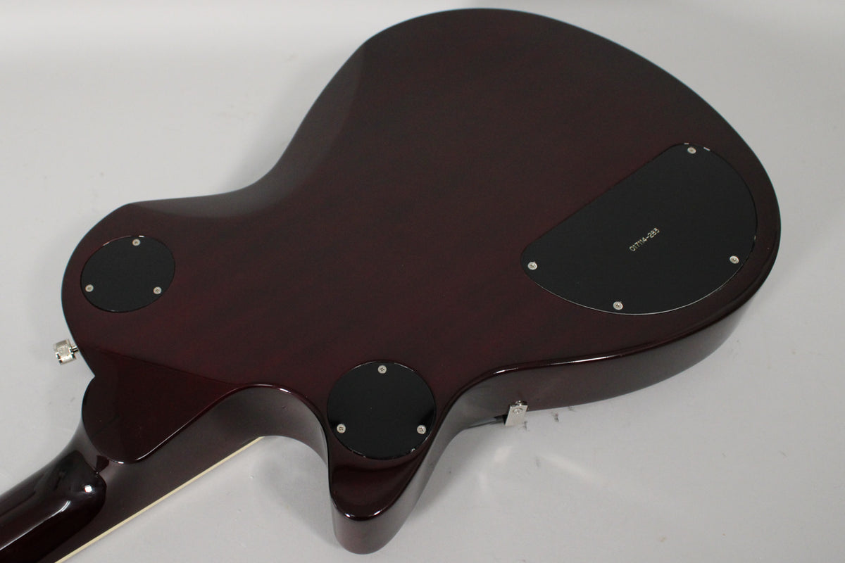 The guitar's transparent red back, angled from the neck to the lower bout, shows three black control cavity covers.