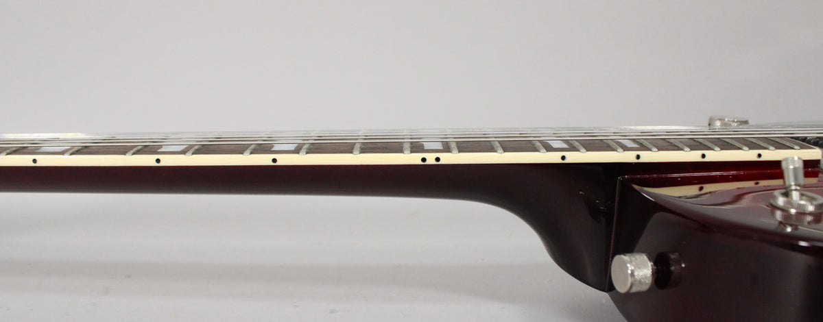 The guitar's transparent red neck and fretboard with block inlays are visible from the side, showing the neck joint and a control knob.