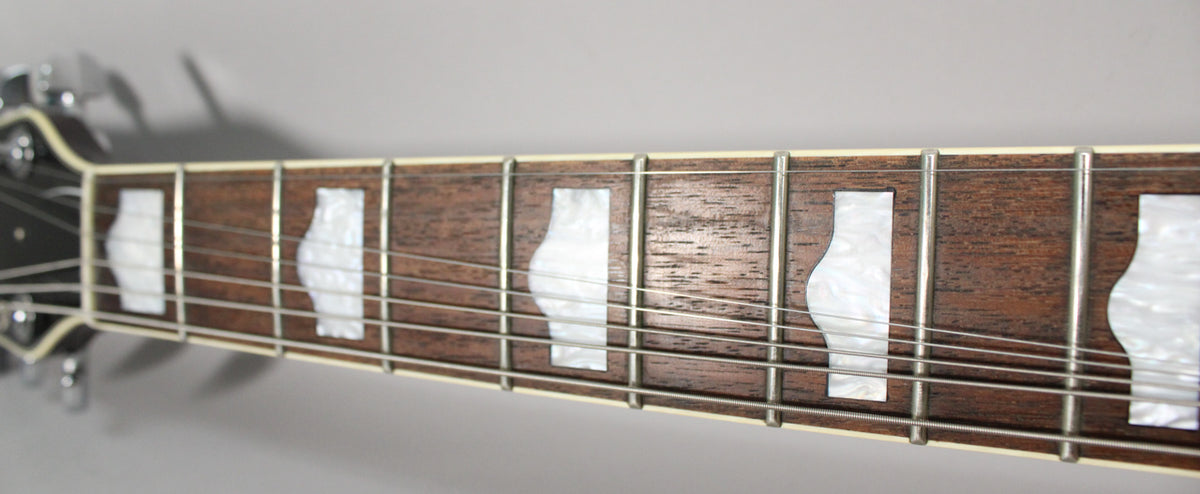 Close-up of the guitar's dark brown fretboard with white pearloid thumbnail inlays, showing light wear on the frets and wood.