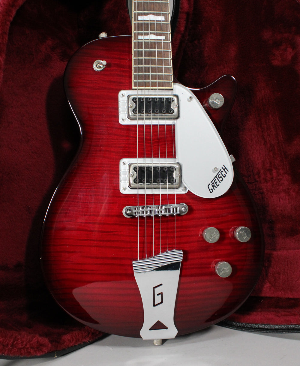 Full view of a transparent red electric guitar with a flamed maple top, two humbuckers, a white pickguard, and chrome hardware.