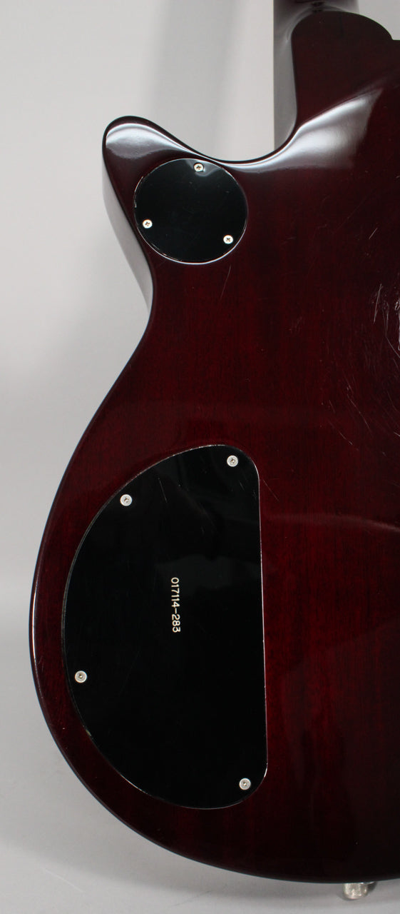 The guitar's transparent red back shows light scratches, with two black control cavity covers secured by silver screws.