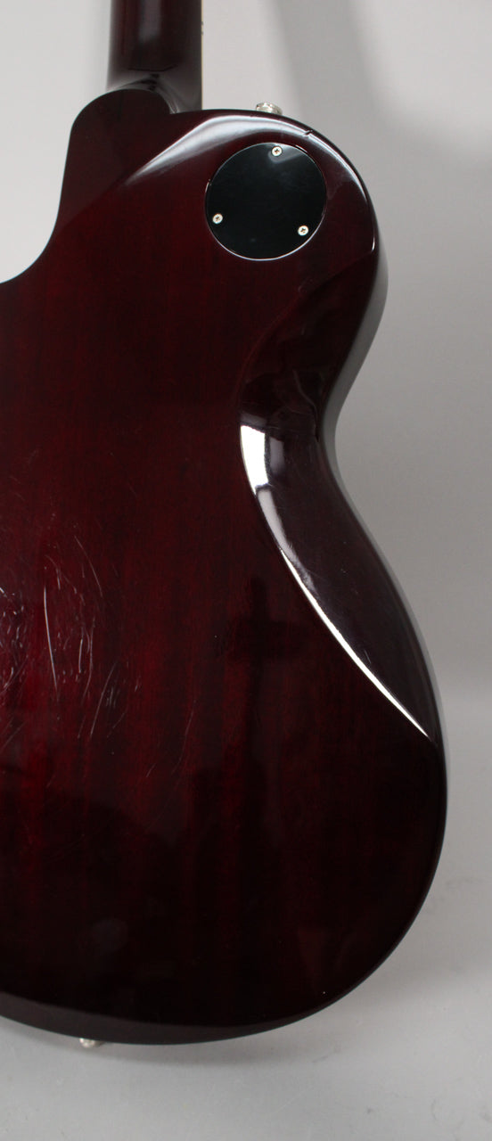 The upper back of the transparent red guitar body, showing a black circular control plate and many light scratches on the glossy finish.