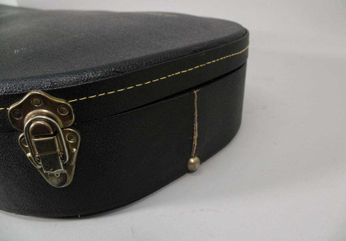 Close-up of the black hard shell case's lower right side, showing a tarnished gold latch and a worn, frayed edge with a brass foot.