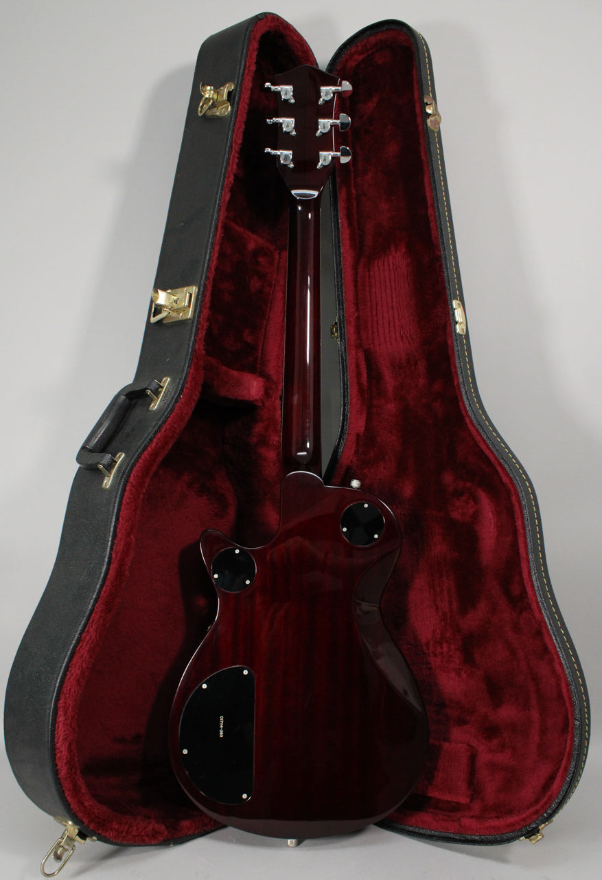 The transparent red guitar is seen from the back, resting in its open black hard case with a deep red plush interior.