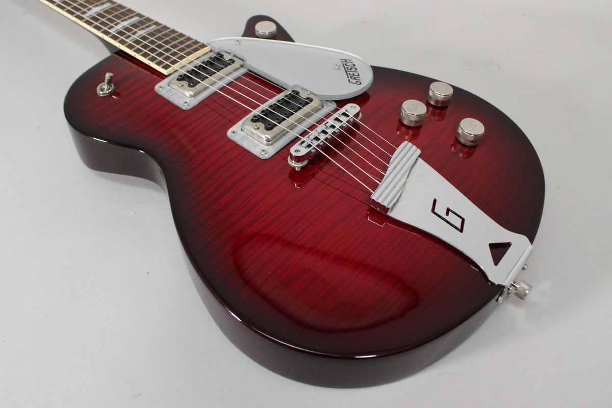 The transparent red electric guitar's body and neck are angled, showing its chrome hardware, pickups, and pickguard.