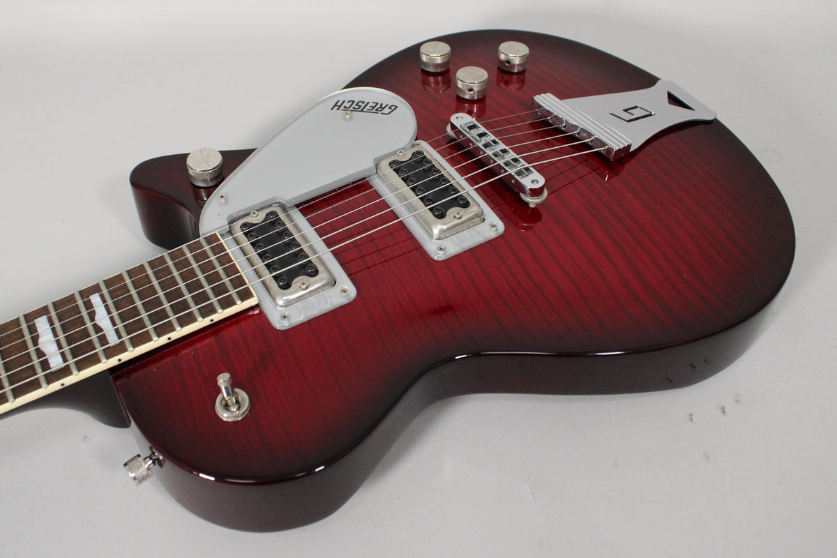 The transparent red electric guitar, angled from the lower left, shows its flamed top, two humbuckers, and a silver pickguard.