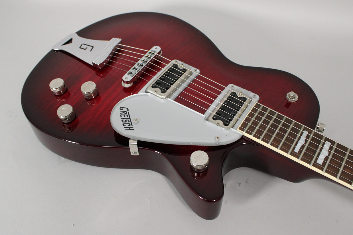 Angled view of a transparent red electric guitar with a silver pickguard, two humbucker pickups, and four chrome control knobs.