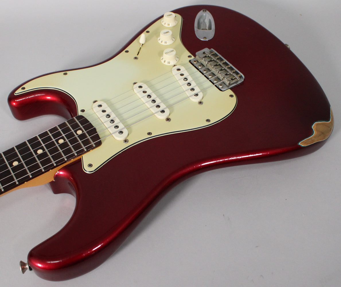 Candy Apple Red Stratocaster body, angled from the neck to the lower bout, showing a worn cream pickguard, three single-coil pickups, and exposed wood on the lower horn.
