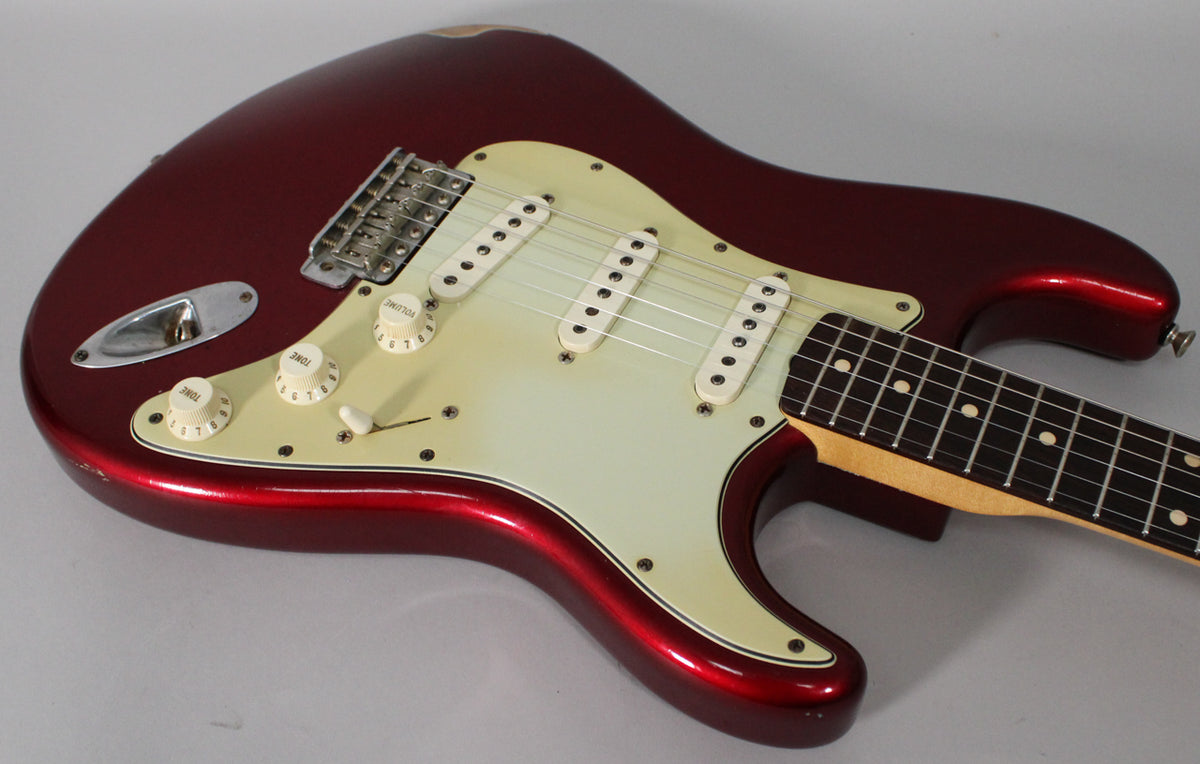 Candy Apple Red Stratocaster body, angled from the lower bout, showing the aged white pickguard, three single coils, and controls.