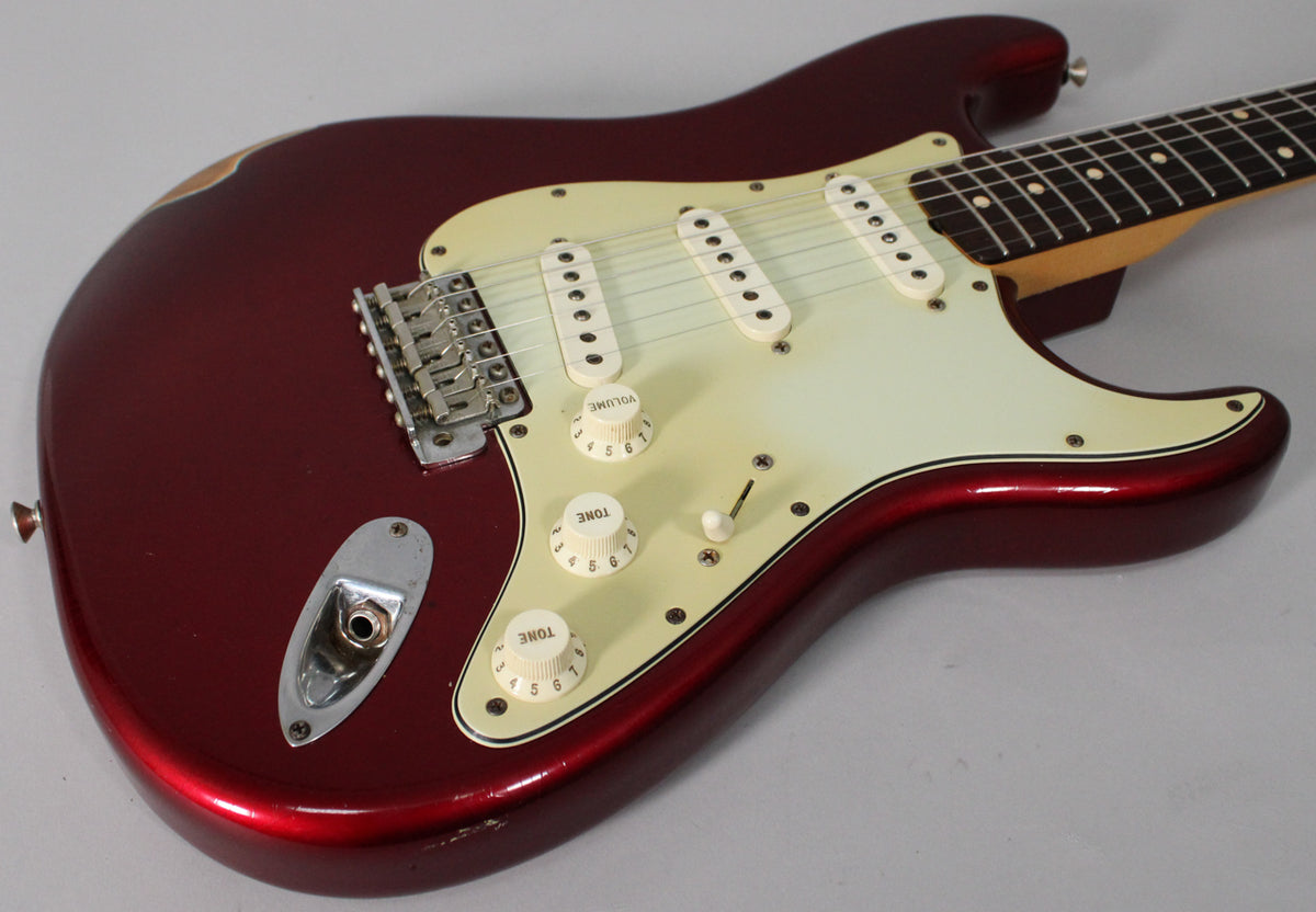 Candy Apple Red Stratocaster body, angled from the lower bout, showing the aged white pickguard, three single-coil pickups, and relic wear.