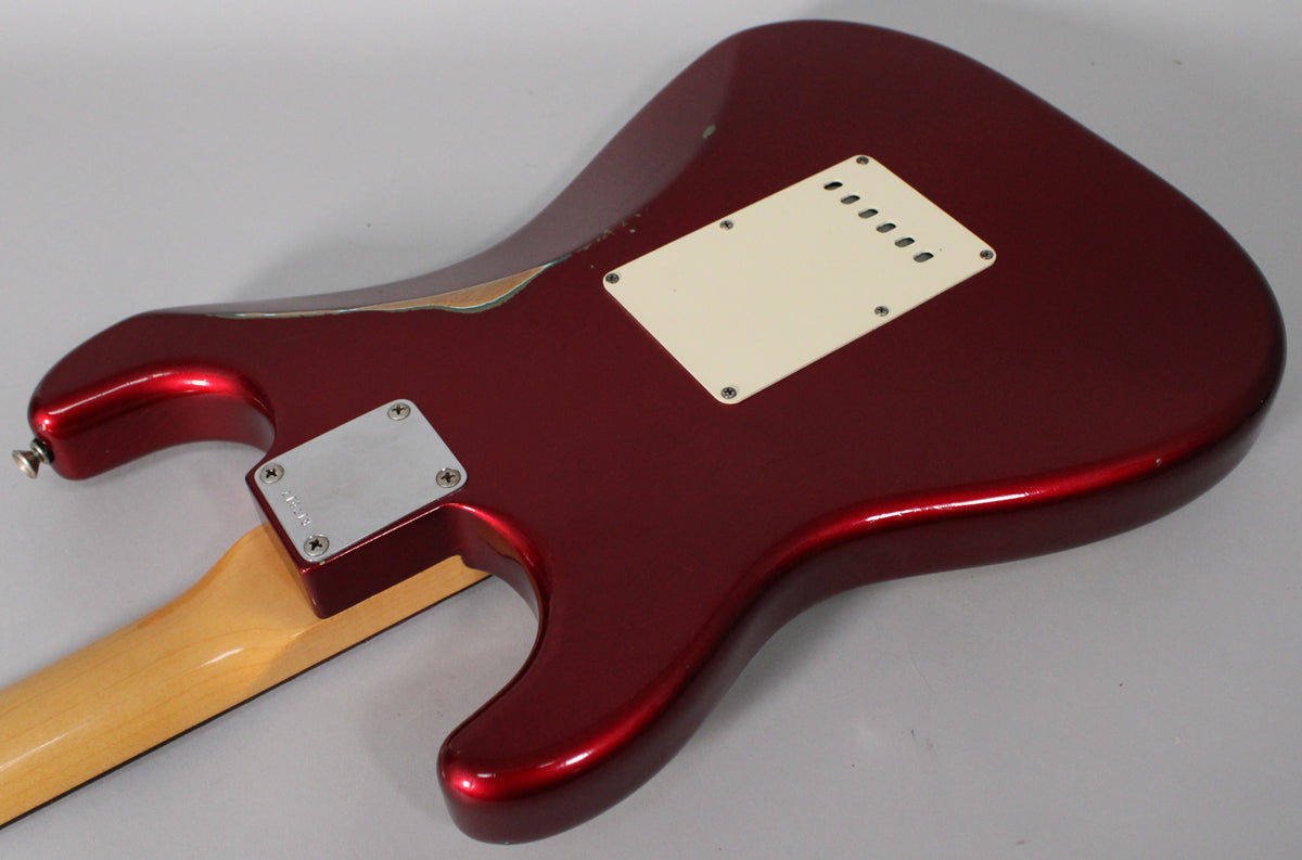 The back of the Candy Apple Red body shows a cream tremolo cover, a chrome neck plate, and significant finish wear on the upper horn.