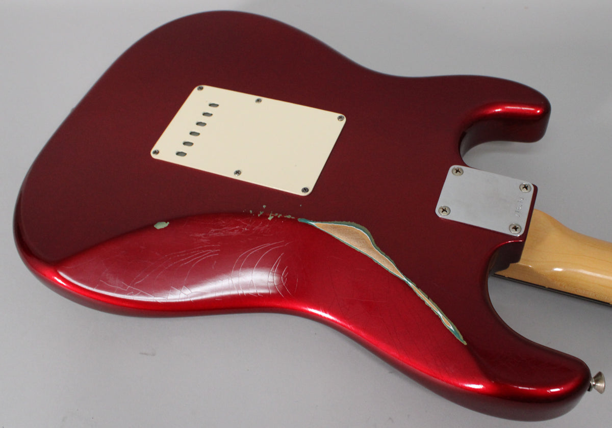 The guitar's back shows a Candy Apple Red finish with heavy wear, revealing wood and green primer, plus a cream tremolo cover.