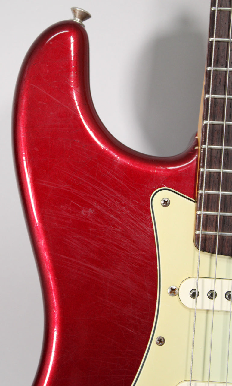 Close-up of the upper bout of a metallic red guitar, showing heavy scratching, finish checking, and a cream pickguard.
