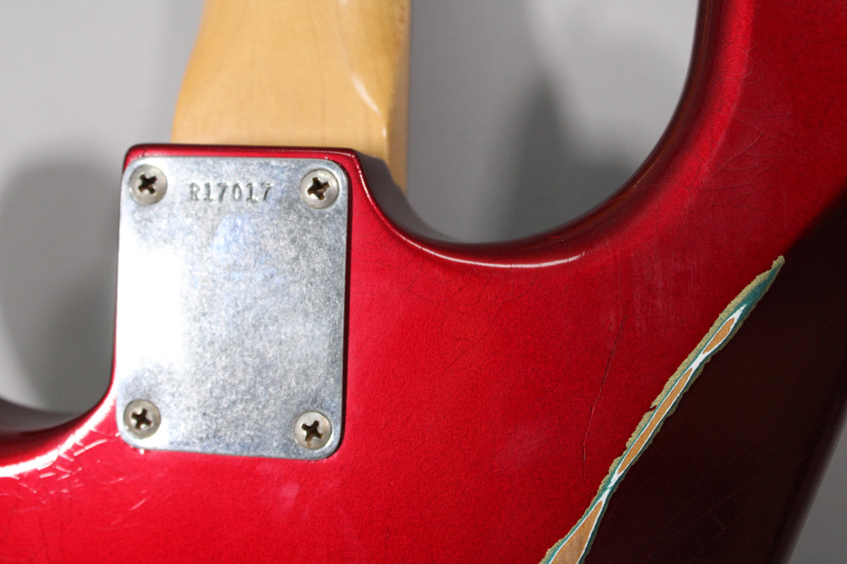 Close-up of the guitar's Candy Apple Red body and neck joint, showing a metal neck plate with serial R17017 and heavy paint chipping.