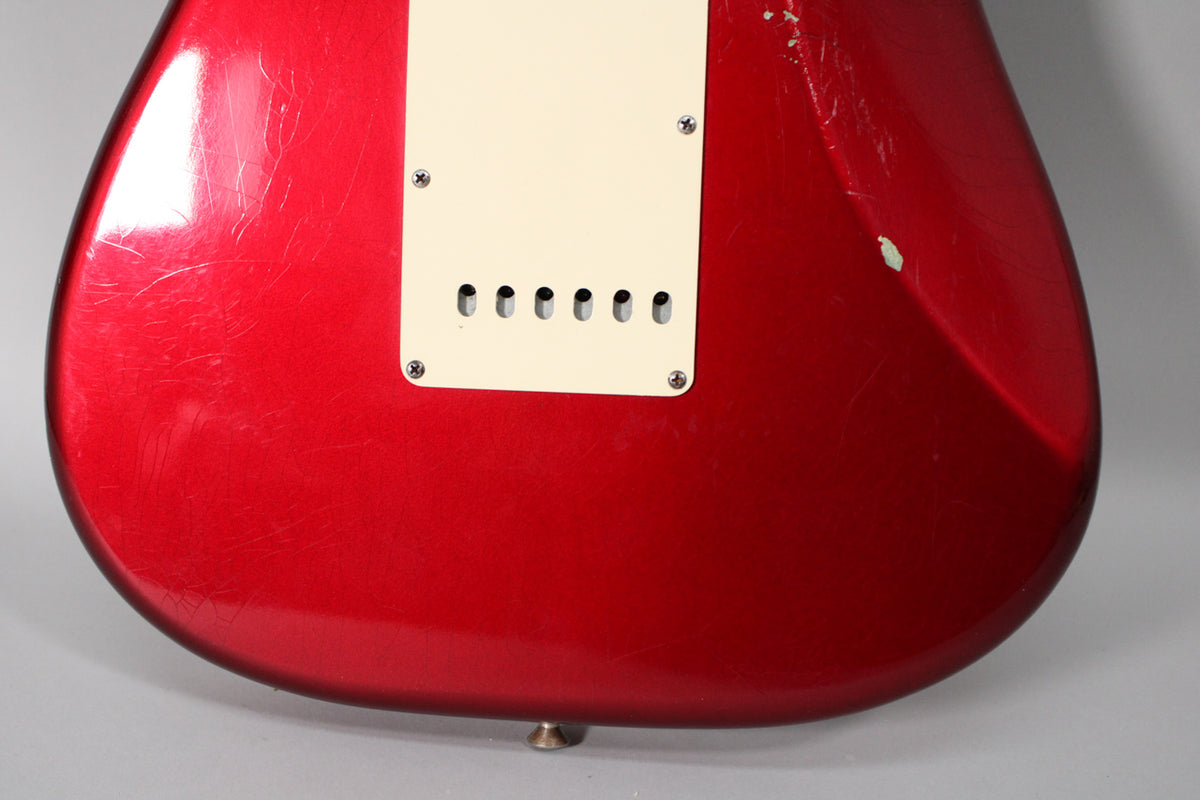 The back of a red metallic guitar body shows a cream tremolo cover, heavy finish checking, and a chip near the upper horn.