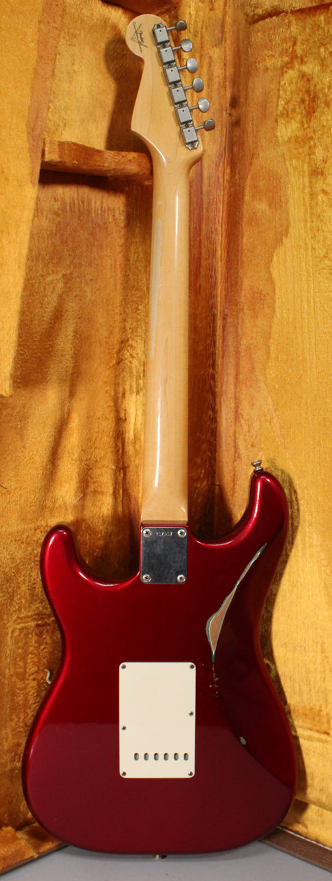 The back of a red Stratocaster with a maple neck, showing a large paint chip on the upper bout and a cream tremolo cover.