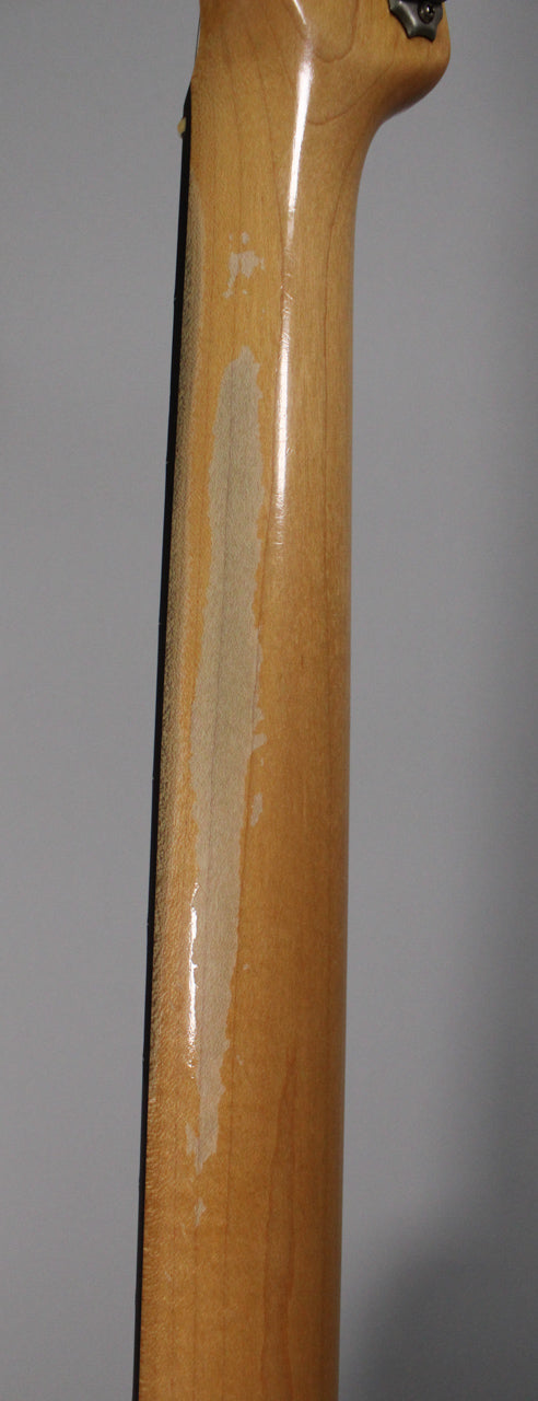 The guitar's maple neck, viewed from behind, shows significant finish wear and wood exposure along its length.