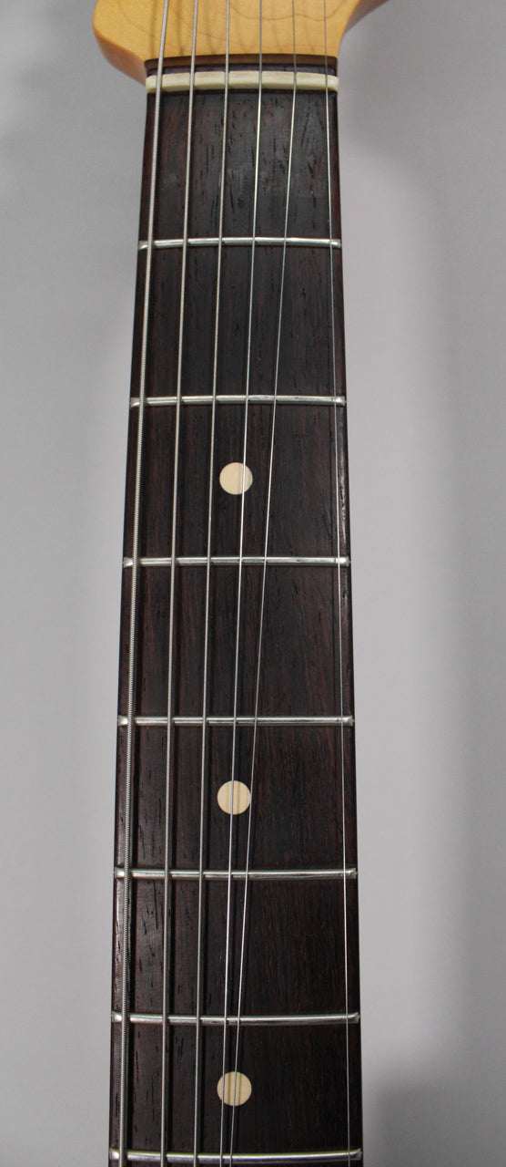 Close-up of the dark rosewood fretboard with light circular inlays, silver frets, and six strings, viewed from above.