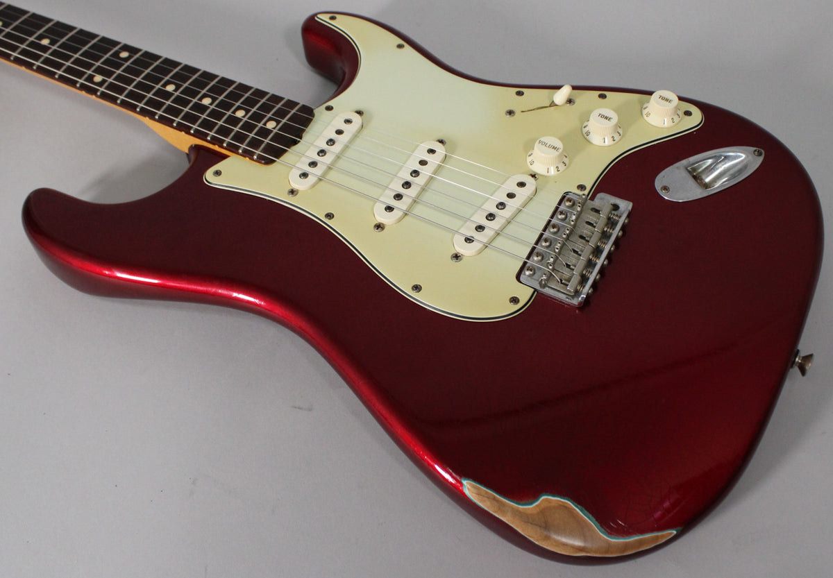 The Candy Apple Red Stratocaster body, with a cream pickguard and pickups, shows significant wear on the lower bout, exposing wood.