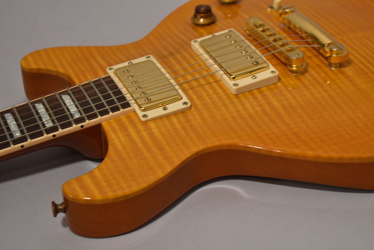 Close-up of the amber flamed maple body, showing gold humbuckers with cream surrounds, gold bridge, and fretboard with trapezoid inlays.