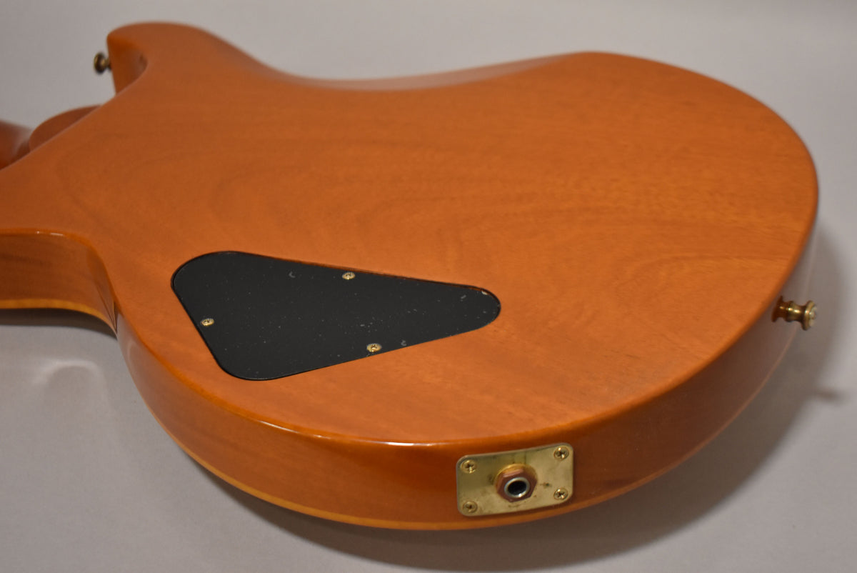 The guitar's amber-finished back, angled from the neck joint to the lower bout, shows a black control cavity cover and a gold output jack plate.