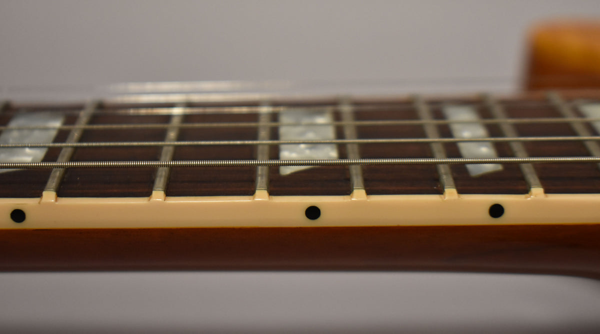 Close-up of the guitar's dark fretboard with trapezoid inlays, showing the cream binding and black side dots.