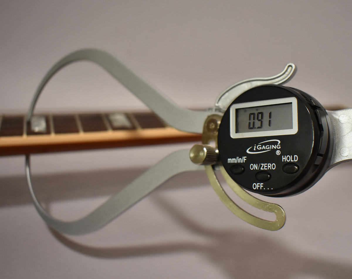 A digital caliper measures the fret height at 0.91mm on the guitar's dark rosewood fretboard with trapezoid inlays.