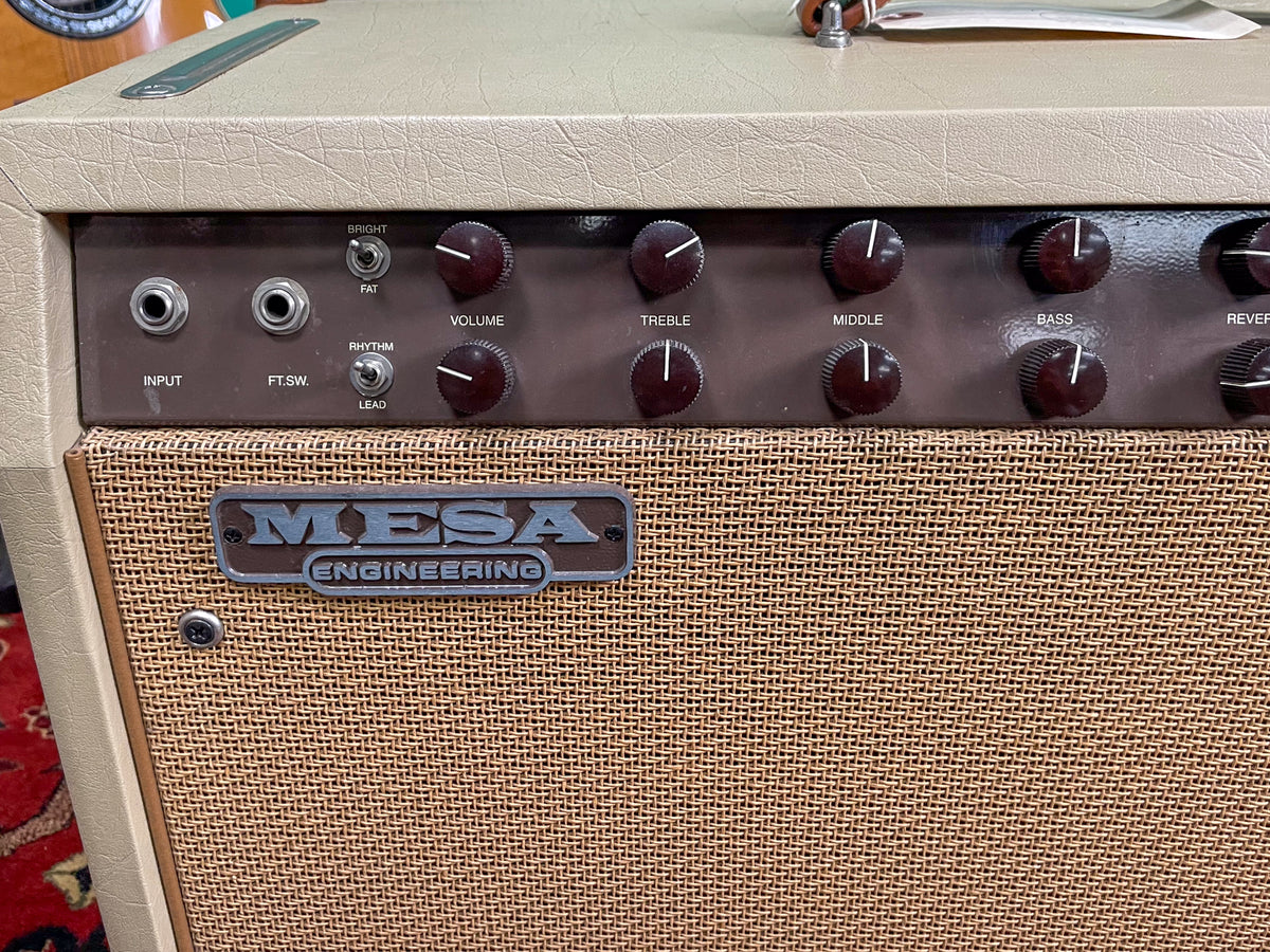 Close-up of the tan combo amp's dark brown control panel with two rows of dark brown knobs and toggle switches, above a woven grille.