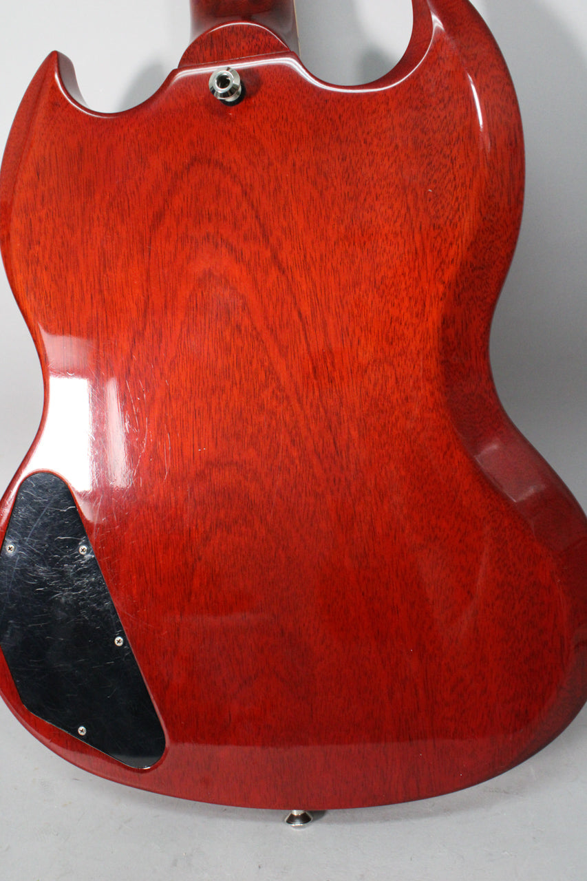 The cherry red guitar's back shows wood grain, a black control cavity cover with scratches, and a strap button at the bottom.