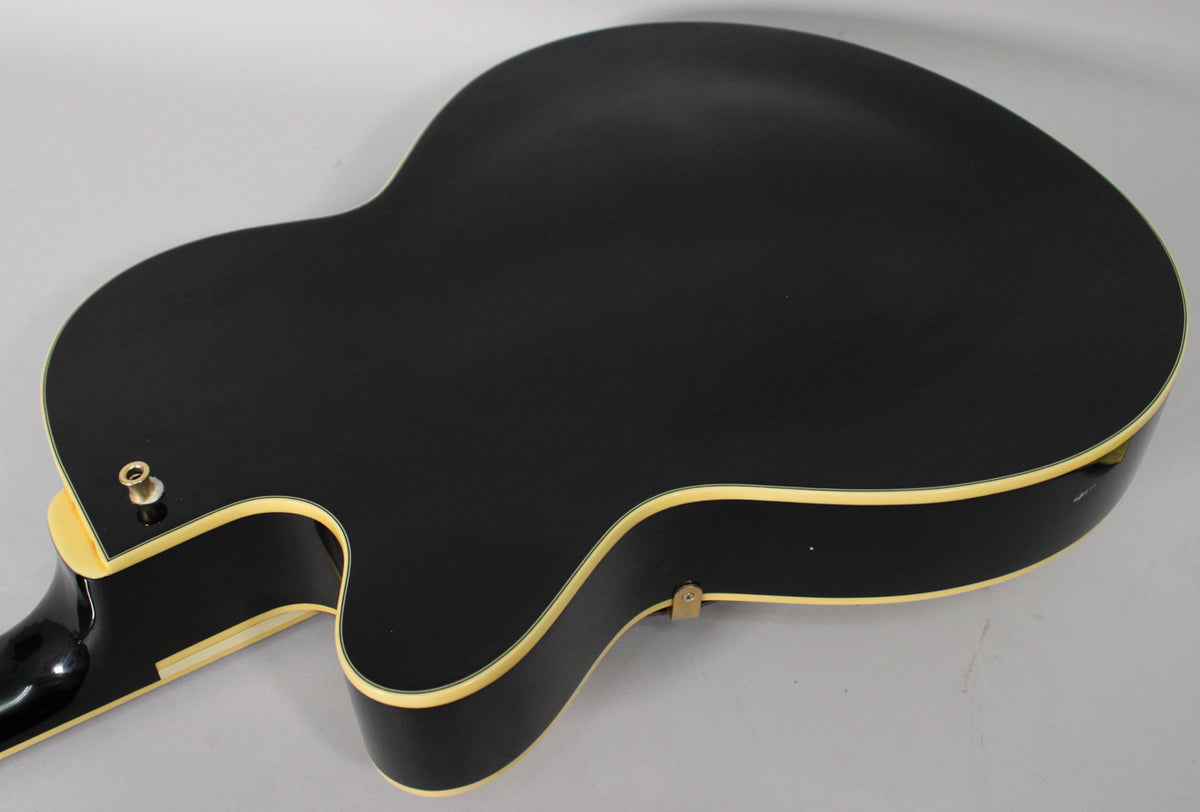 The guitar's black back and sides are shown from above, with cream binding and a strap button visible on the lower bout.