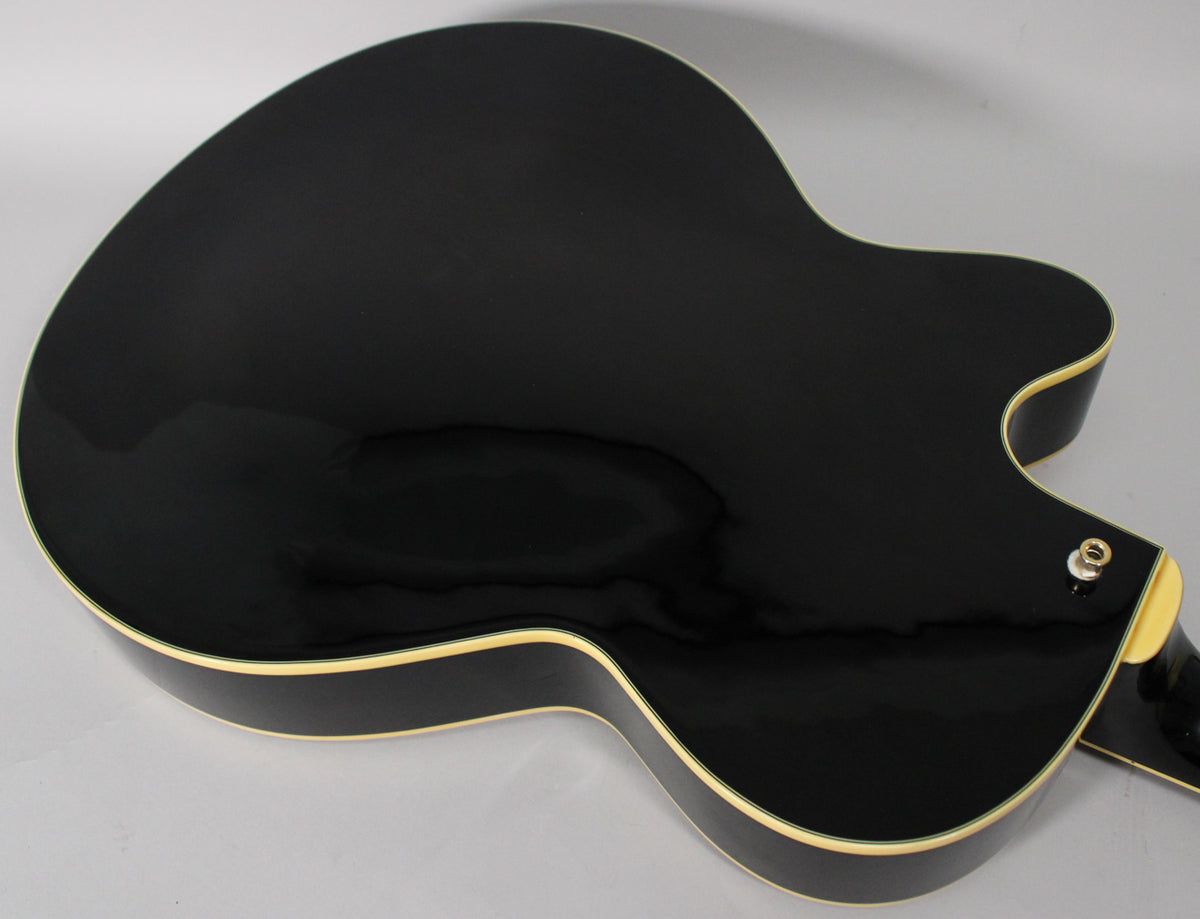 The guitar's glossy black back and sides are visible, with cream binding and a chrome output jack on the lower bout.