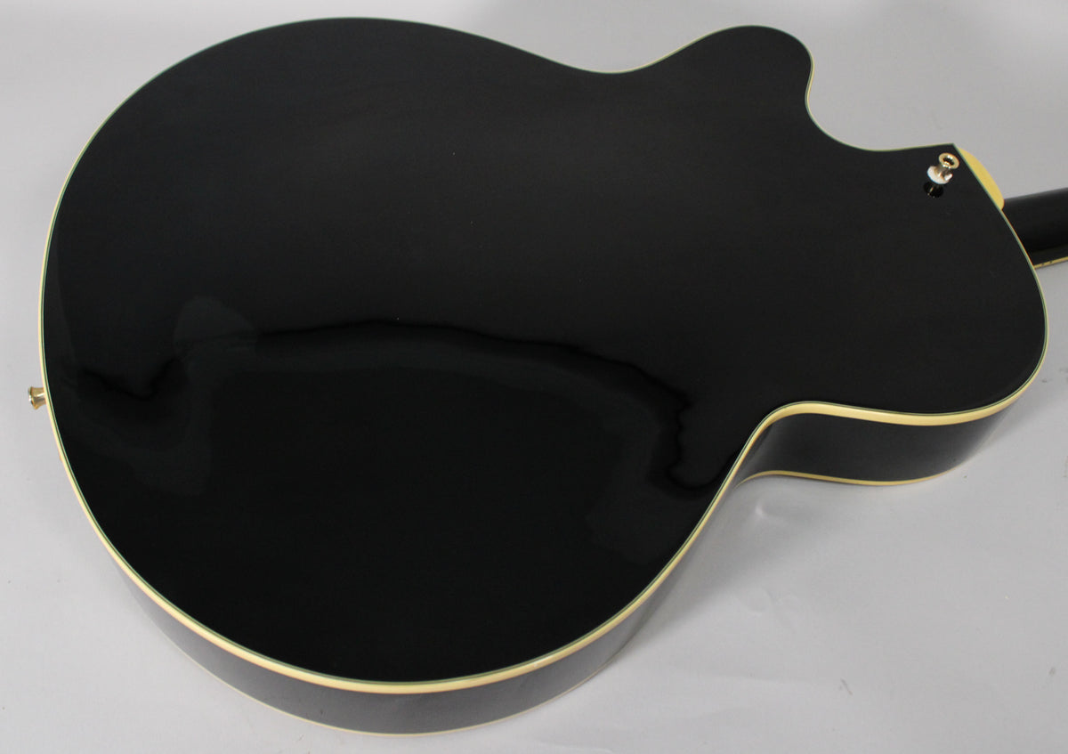 The back of a black hollow-body electric guitar, showing light reflections on its glossy finish and cream binding along the edges.