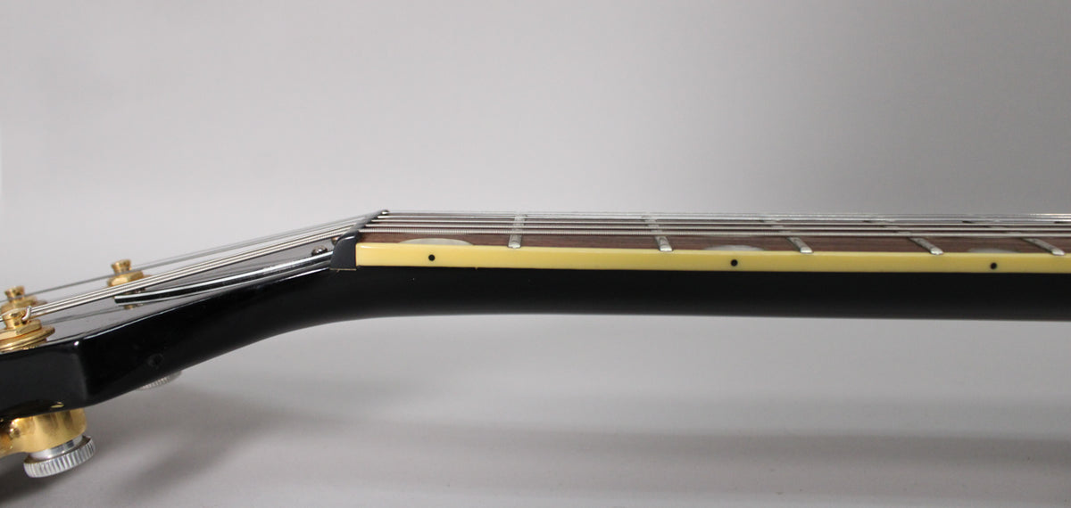 Close-up of the guitar neck from the side, showing the dark fretboard, cream binding, and gold tuning pegs.