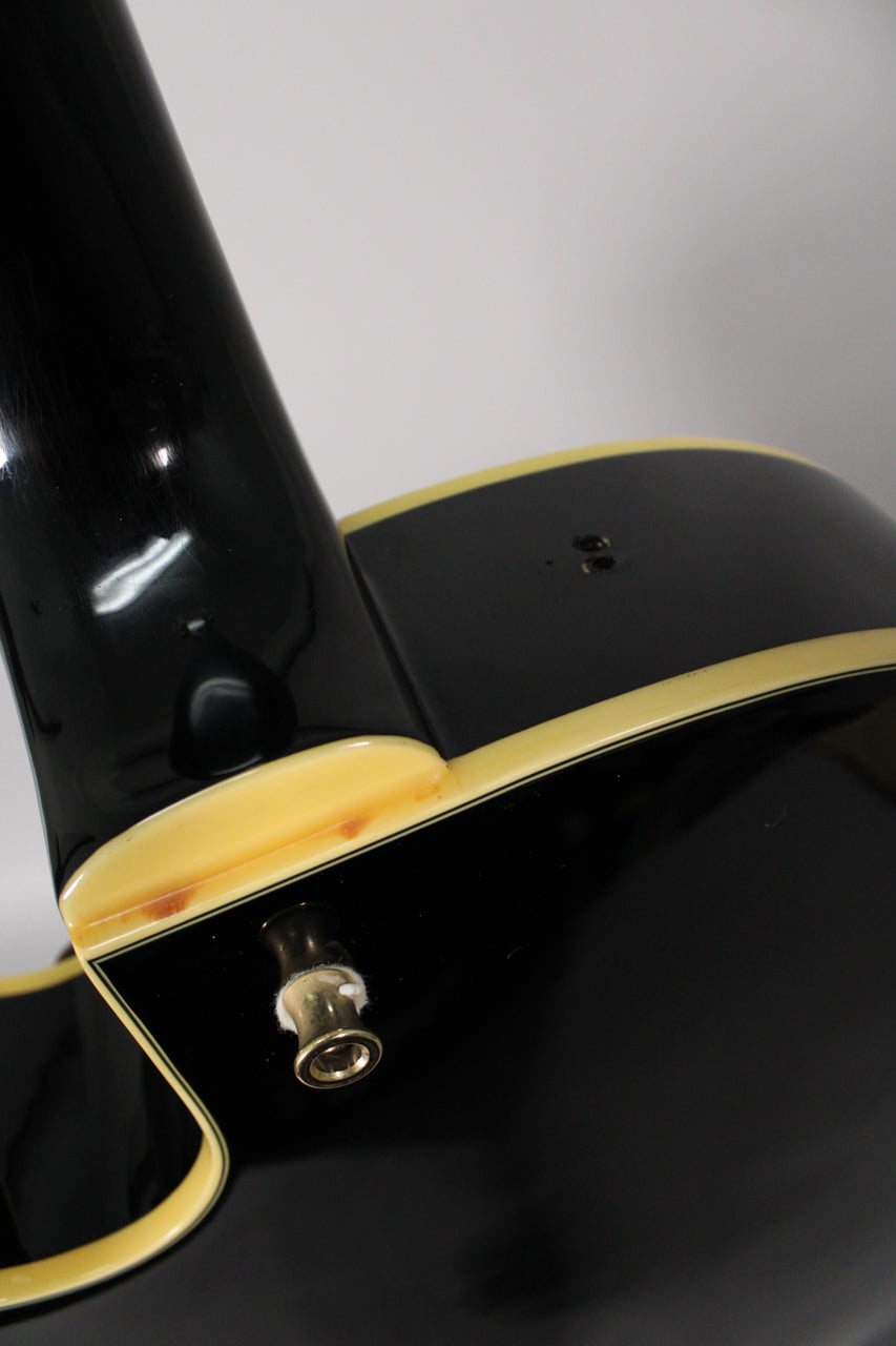 Close-up of the guitar's black body and neck heel, showing the input jack and cream binding with some visible wear and discoloration.