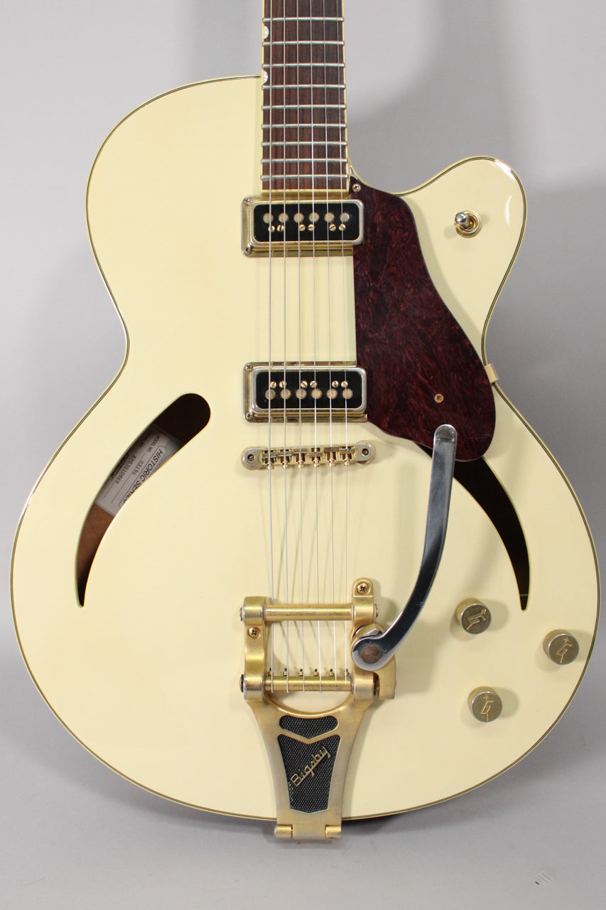 The antique white hollow-body electric guitar is angled slightly, showing its Bigsby vibrato, two P90 pickups, and dark tortoiseshell pickguard.