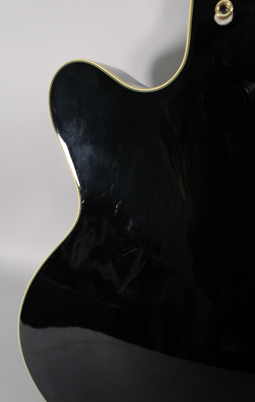 Close-up of the guitar's upper bout from the back, showing a glossy black finish with numerous light scratches and cream binding.