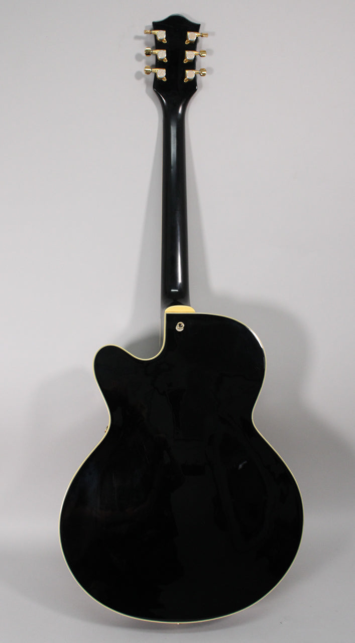 Full rear view of a glossy black hollow-body electric guitar with a single cutaway, cream binding, and gold tuners.