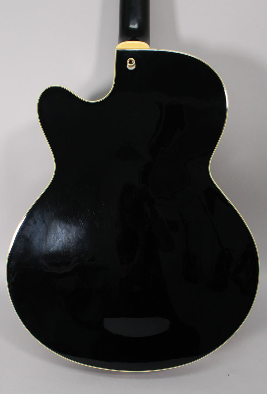 The guitar's glossy black back, with cream binding, shows many light scratches and a strap button on the upper bout.