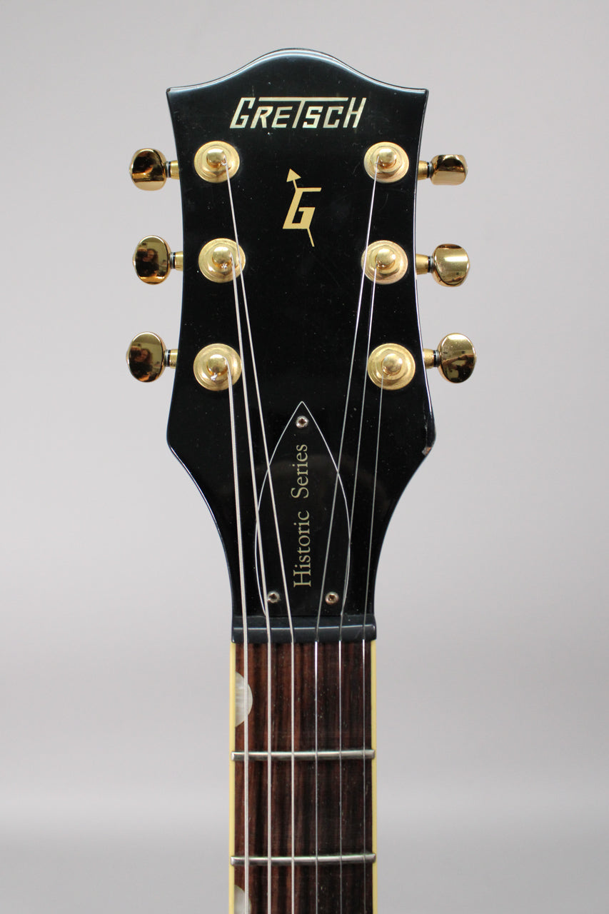 Close-up of the black headstock with gold tuners and "Historic Series" on the truss rod cover, showing some wear on the edges.